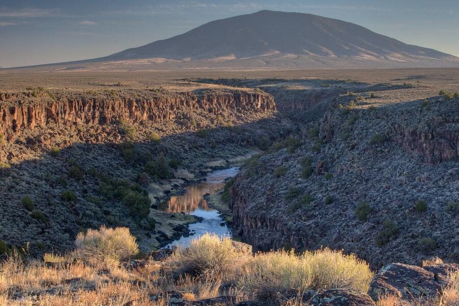 The Rio Grande winding through the gorge in evening light, with a mountain on the horizon